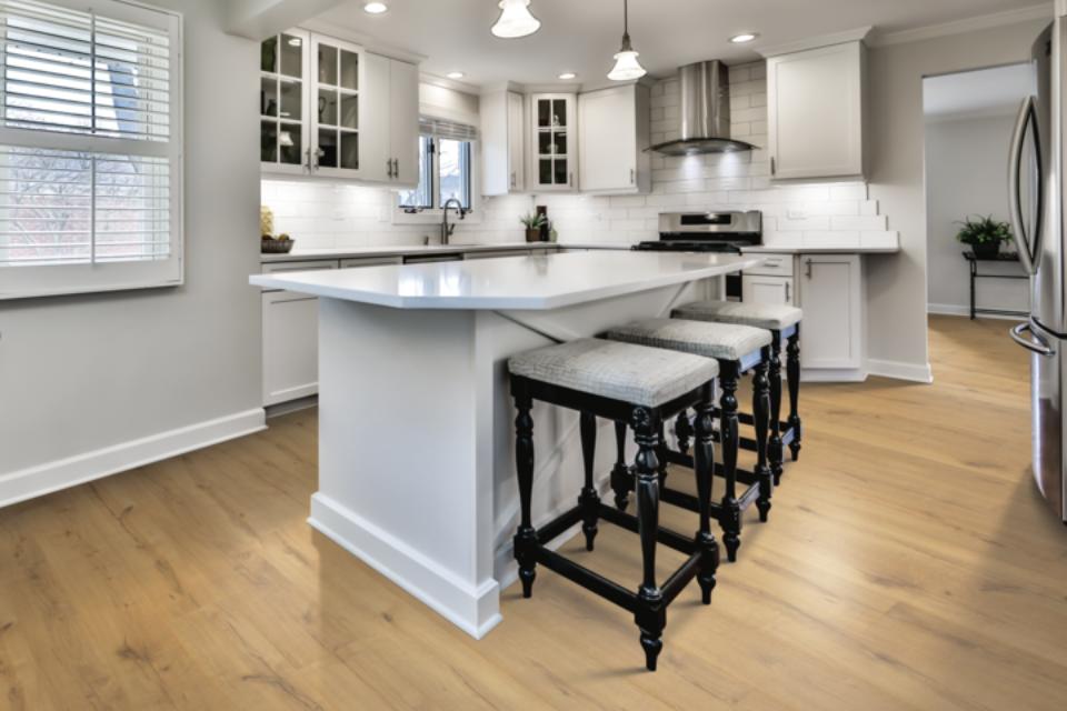 Warm toned laminate flooring in kitchen with white counters, black stools, and white tile backsplash.